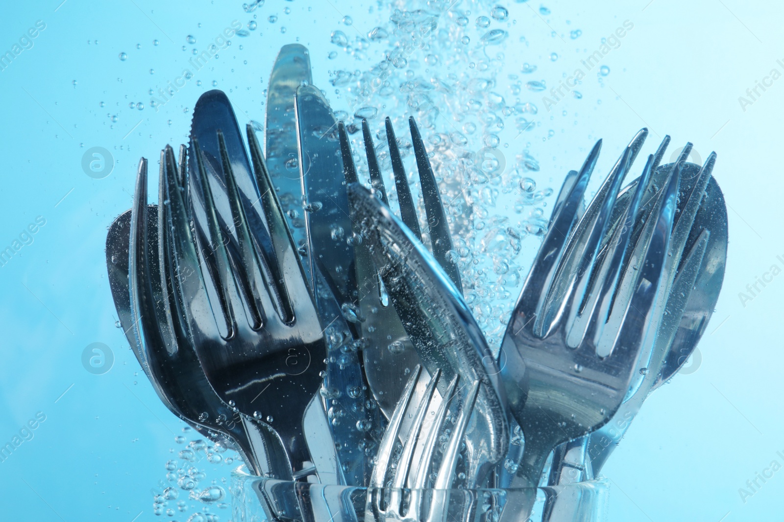 Photo of Washing silver cutlery in water on light blue background