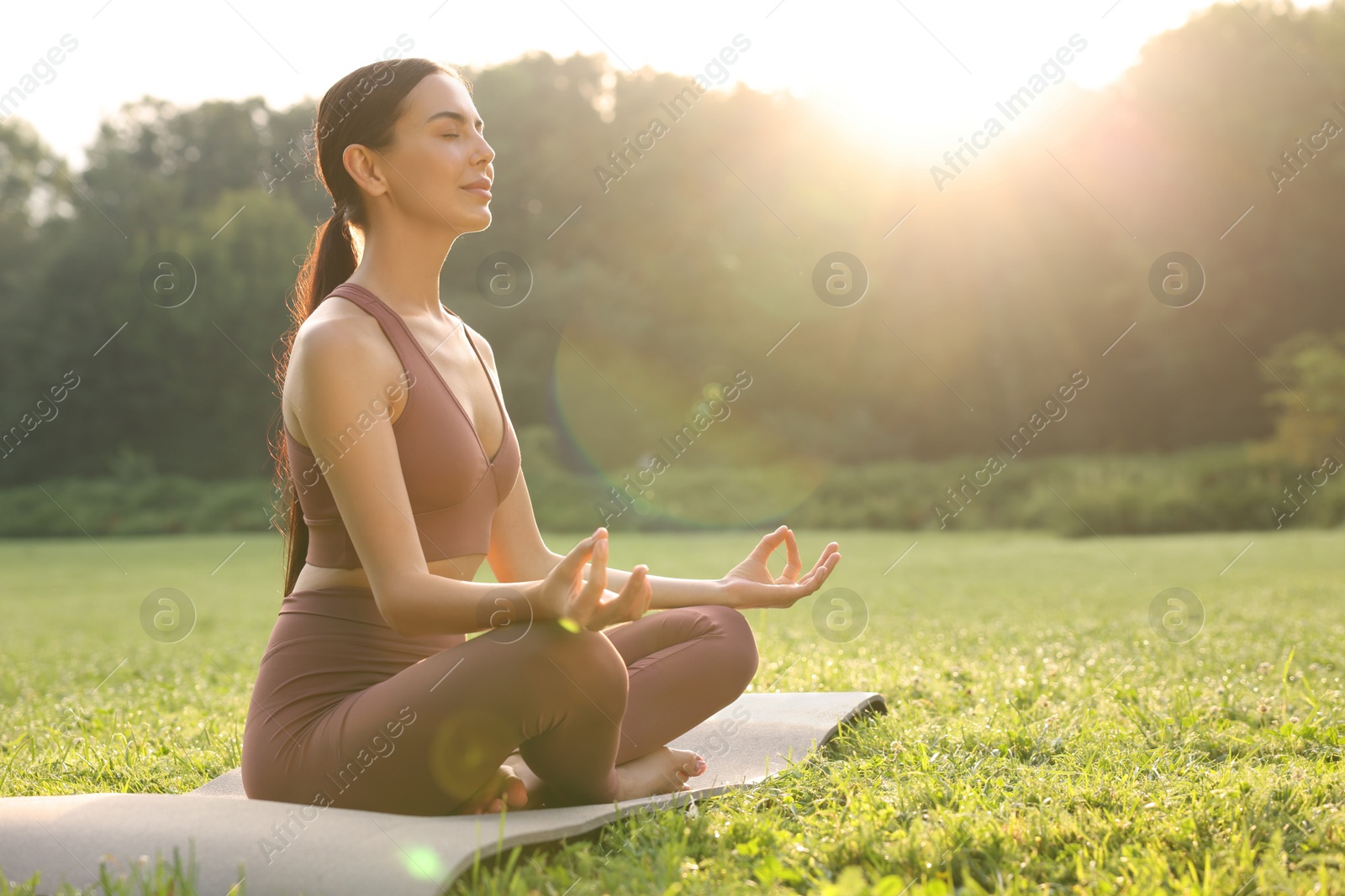 Photo of Beautiful young woman practicing Padmasana on yoga mat outdoors, space for text. Lotus pose