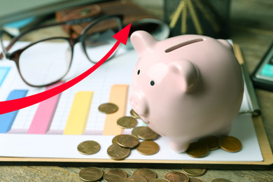 Pink piggy bank with coins on wooden table and growing arrow