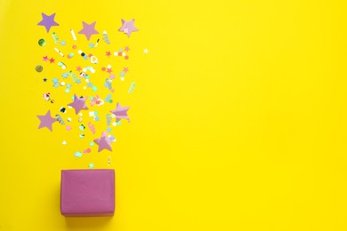 Photo of Different shiny confetti and box on yellow background, flat lay. Space for text