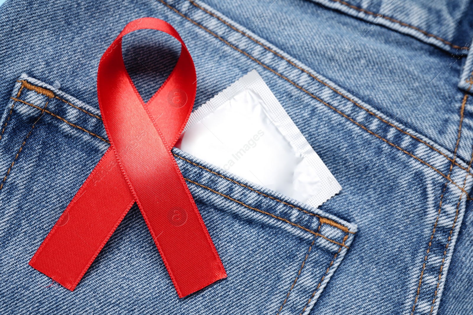 Photo of Jeans with red ribbon and condom, closeup. AIDS disease awareness