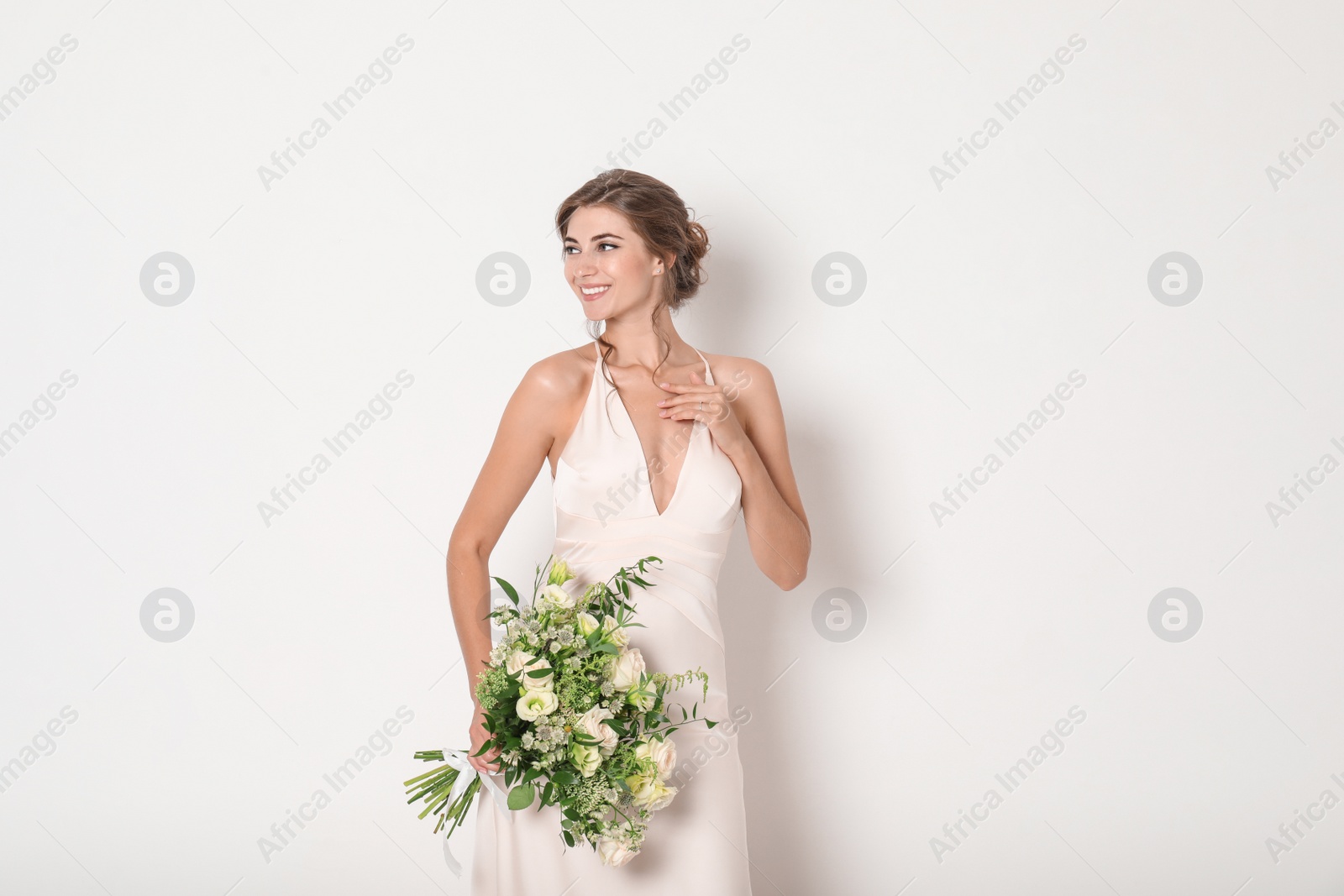 Photo of Young bride wearing wedding dress with beautiful bouquet on light background