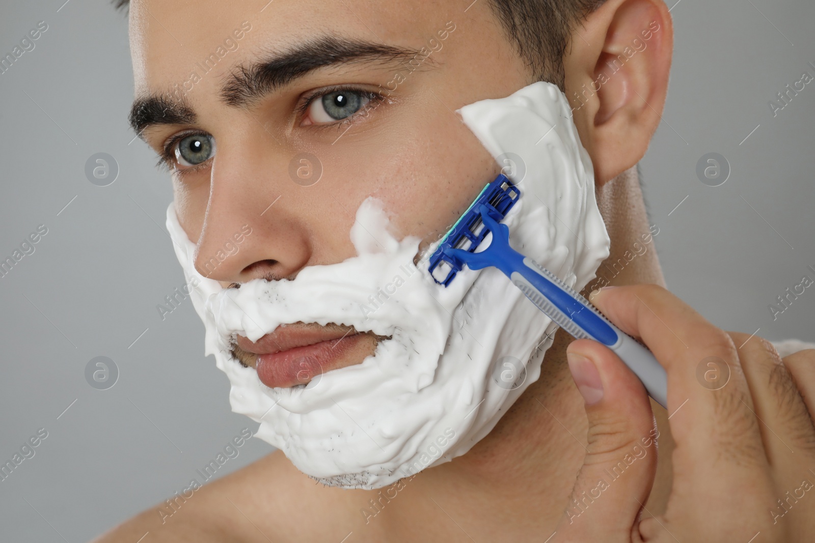 Photo of Handsome young man shaving with razor on grey background, closeup