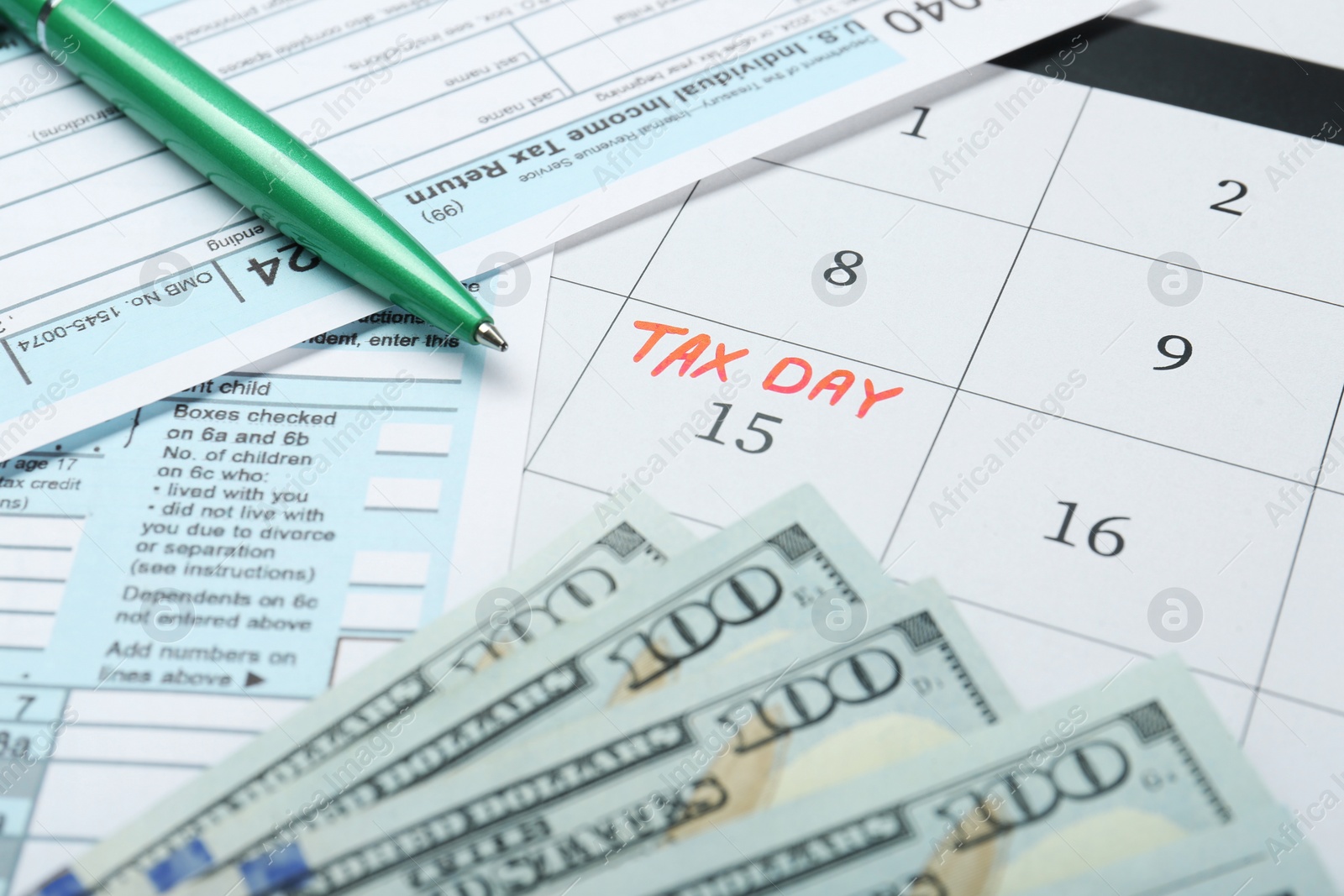 Photo of Tax day. Calendar with date reminder, documents, pen and dollar banknotes on table