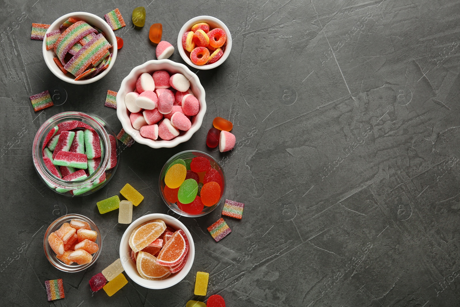 Photo of Flat lay composition with bowls of different jelly candies on black stone background. Space for text