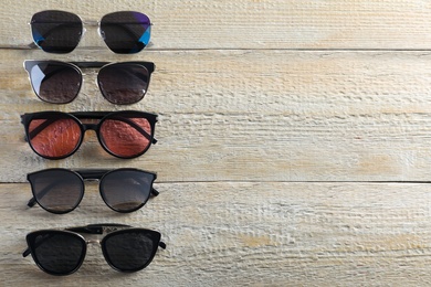 Many stylish sunglasses on wooden background, flat lay. Space for text