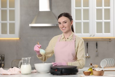 Photo of Young woman cooking delicious crepes in kitchen