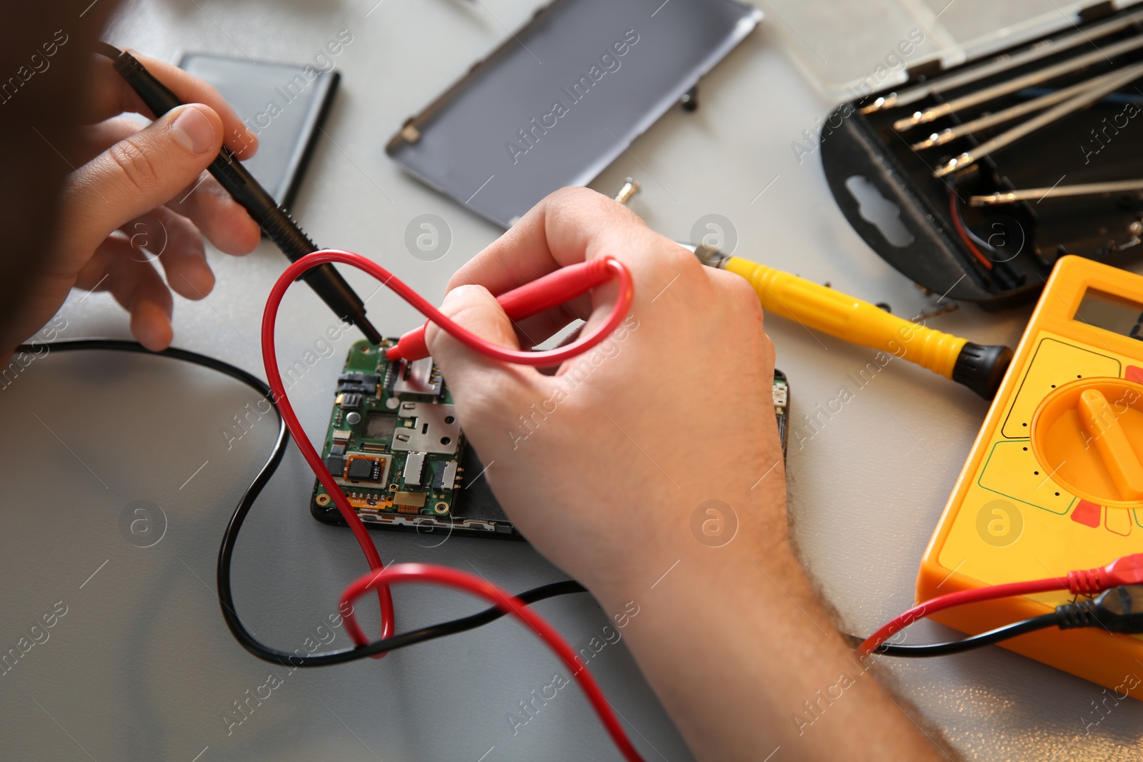Photo of Technician checking mobile phone at table in repair shop, closeup