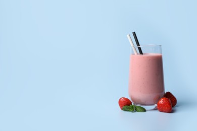 Photo of Glass with delicious berry smoothie and fresh strawberries on light blue background. Space for text