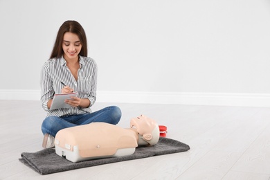 Photo of Woman with notebook near mannequin at first aid class indoors