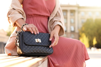 Photo of Young woman with stylish black bag on bench outdoors, closeup
