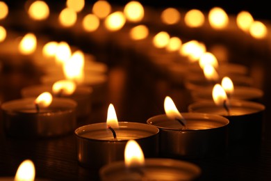 Photo of Burning candles on table in darkness, closeup