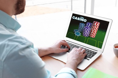Image of Man playing poker on laptop at table, closeup. Casino online