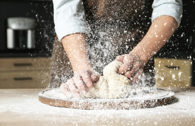 Image of Young woman kneading dough at table in kitchen, closeup