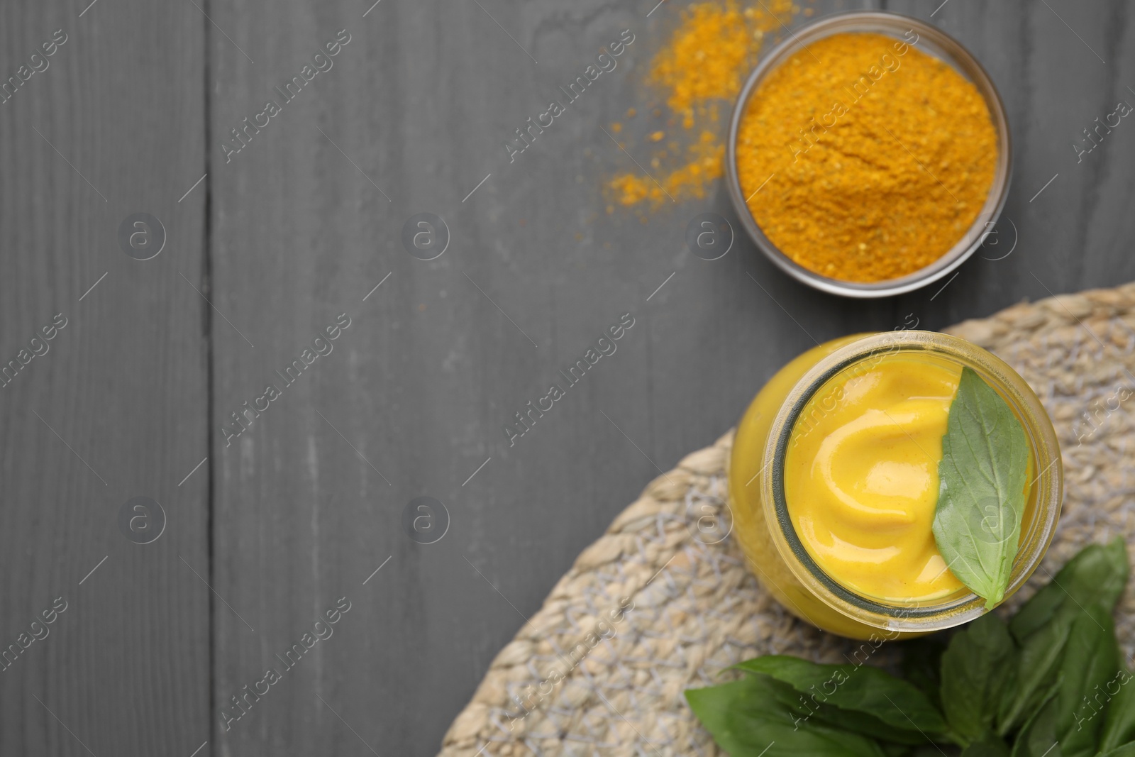 Photo of Tasty curry sauce, powder and basil leaves on grey wooden table, flat lay. Space for text