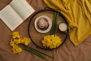 Bouquet of beautiful daffodils, bun and coffee on bed, top view