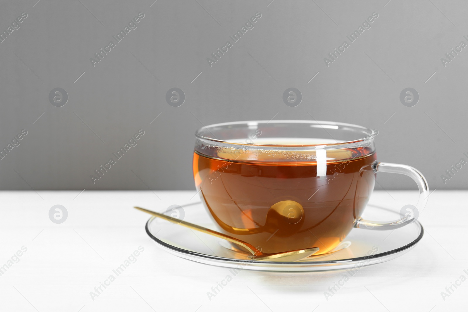 Photo of Glass cup of tea and spoon on white table. Space for text