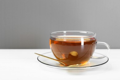 Photo of Glass cup of tea and spoon on white table. Space for text