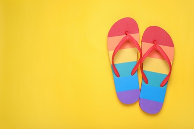 Photo of Rainbow flip flops on yellow background, flat lay with space for text. LGBT pride