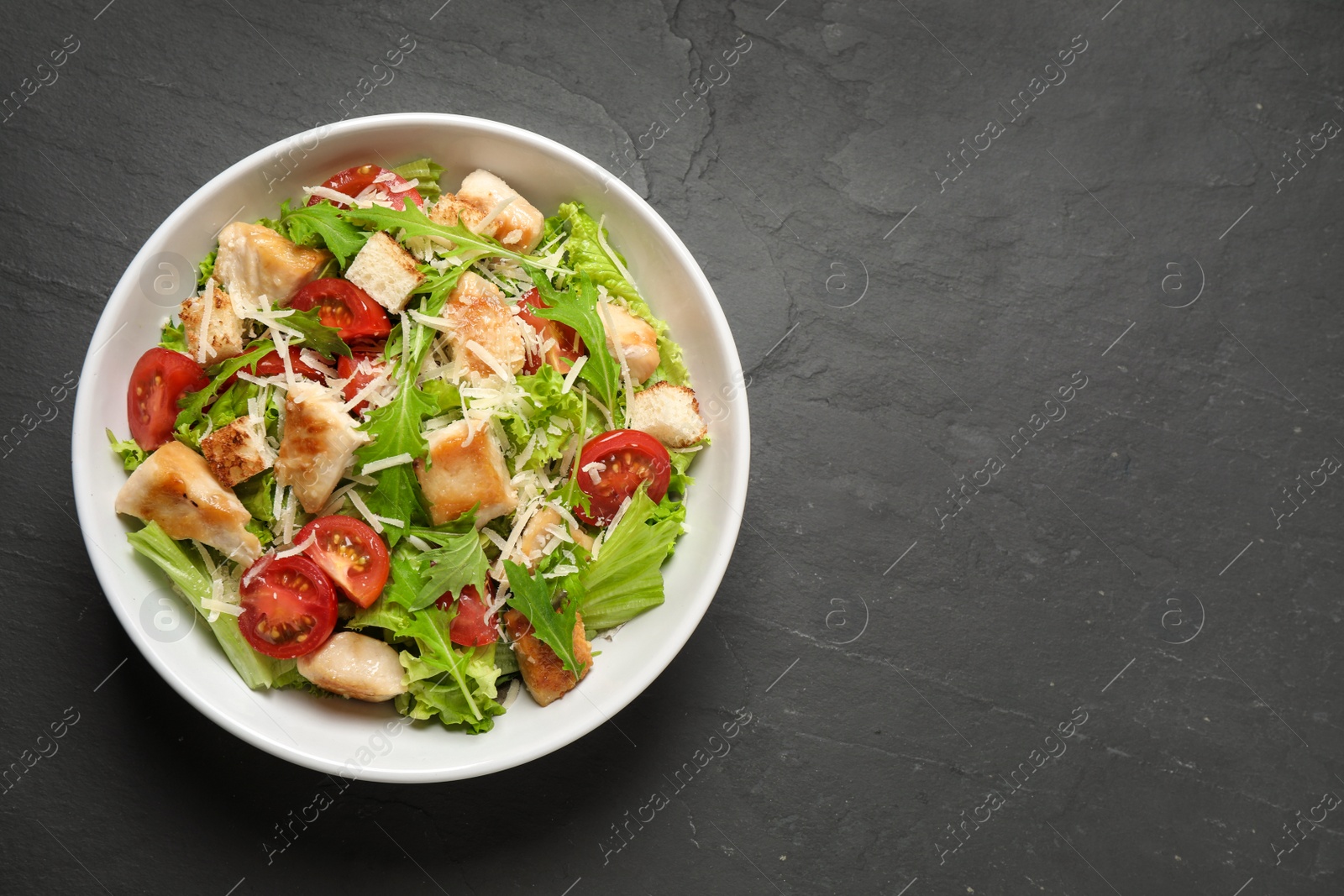 Photo of Delicious fresh Caesar salad on black table, top view. Space for text