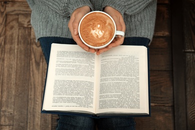 Photo of Woman with cup of coffee reading book at home, top view