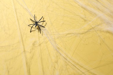 Cobweb and spider on yellow background, top view