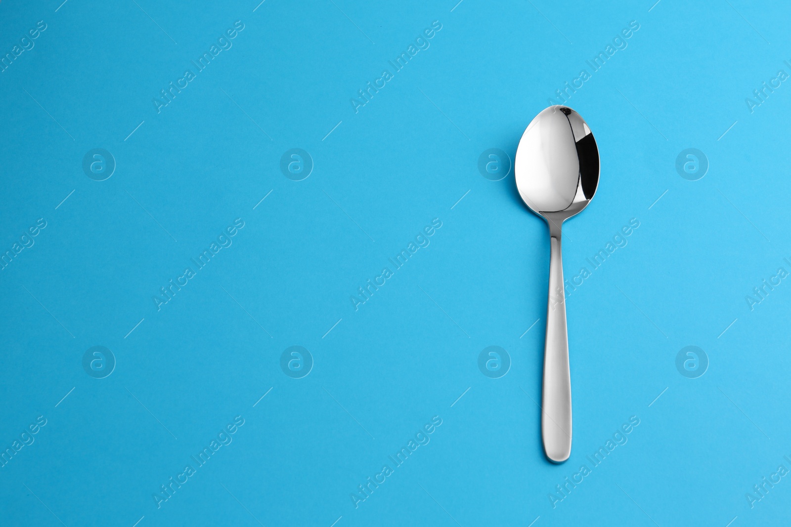 Photo of Clean empty table spoon on blue background, top view. Space for text