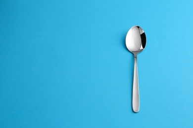 Clean empty table spoon on blue background, top view. Space for text