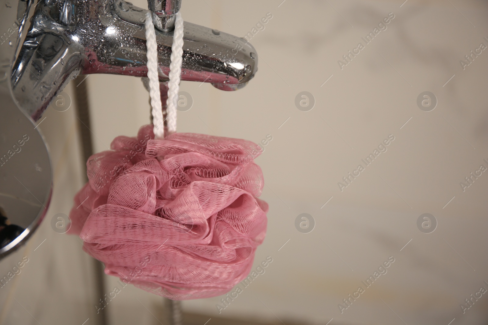 Photo of Pink shower puff hanging on faucet in bathroom, closeup. Space for text