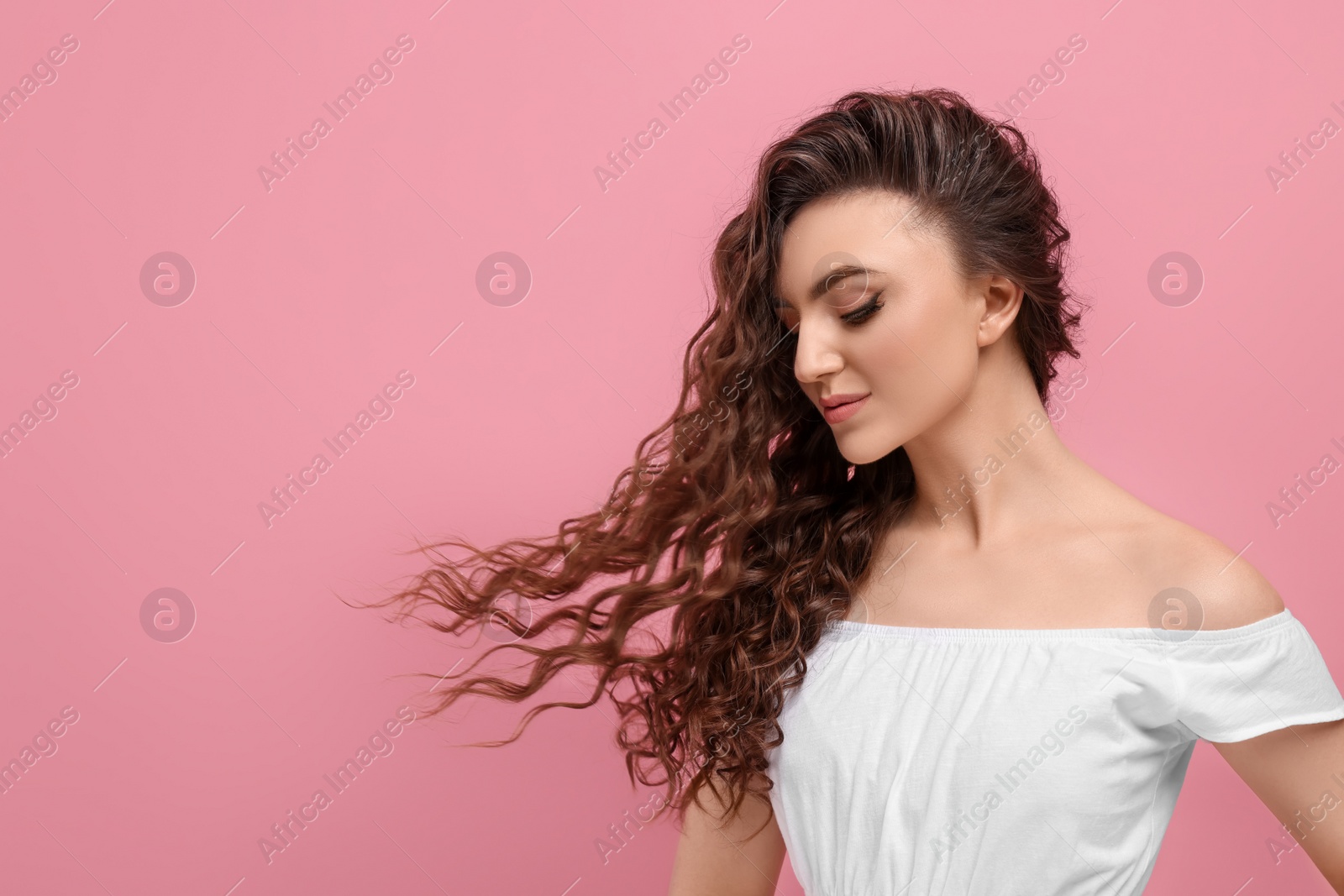 Photo of Beautiful young woman with long curly brown hair on pink background, space for text