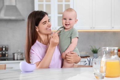Photo of Happy young woman feeding her cute little baby at table in kitchen