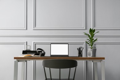 Photo of Stylish workplace with laptop, houseplant and stationery on wooden table near light grey wall