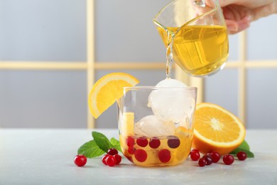 Photo of Woman pouring tasty cocktail into glass with ice balls at light grey marble table, closeup