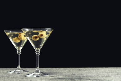 Photo of Martini cocktails with olives on grey table against dark background, space for text