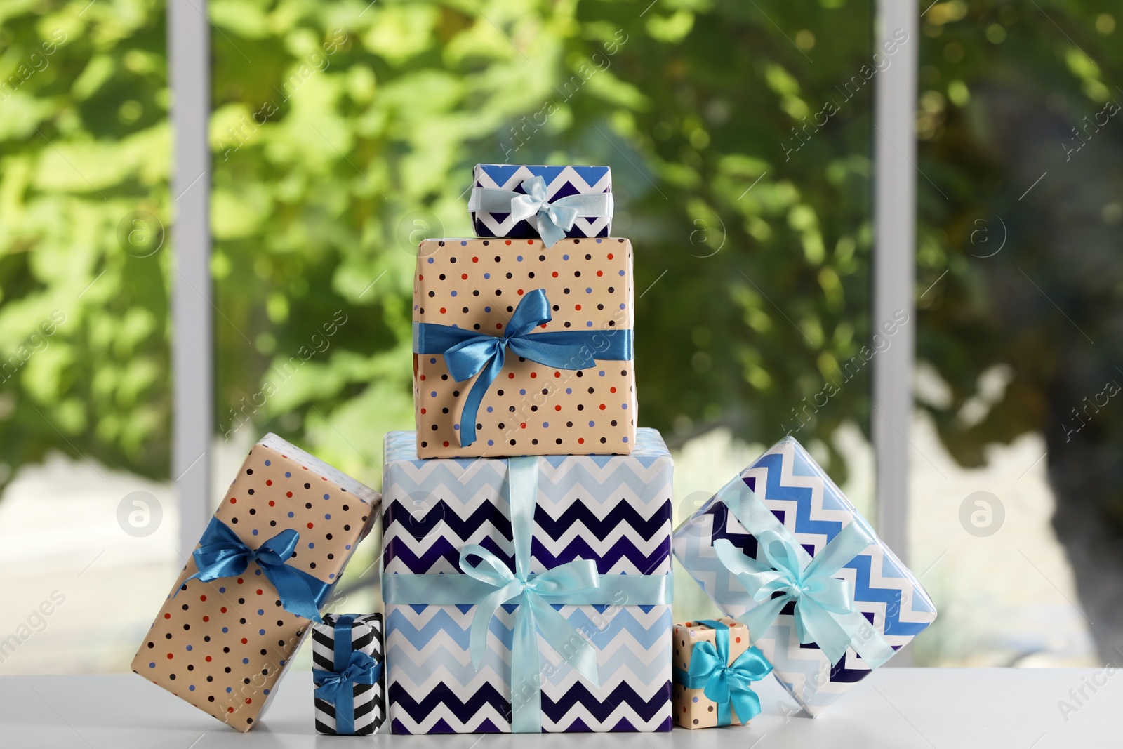 Photo of Many beautifully wrapped gift boxes on white table  near window