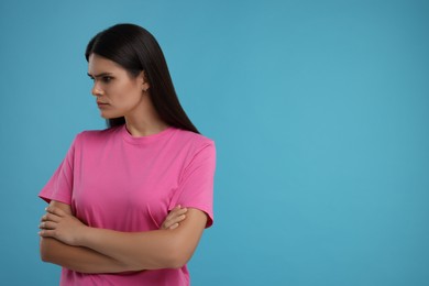 Resentful woman with crossed arms on light blue background, space for text