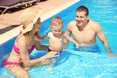 Happy family with little child resting in swimming pool outdoors