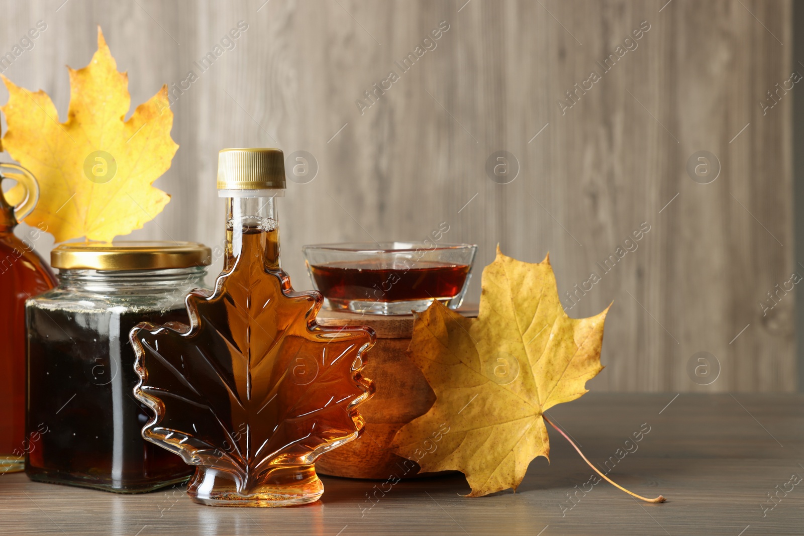 Photo of Bottle and jars of tasty maple syrup on wooden table, space for text