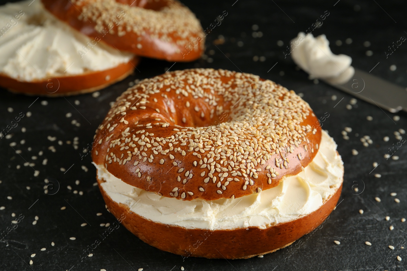 Photo of Delicious bagel with cream cheese on black table, closeup