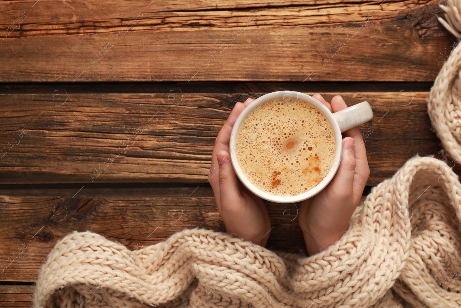 Photo of Woman holding cup of coffee at wooden table, top view with space for text. Cozy winter