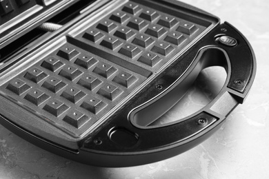 Photo of Modern waffle iron on grey marble table, closeup