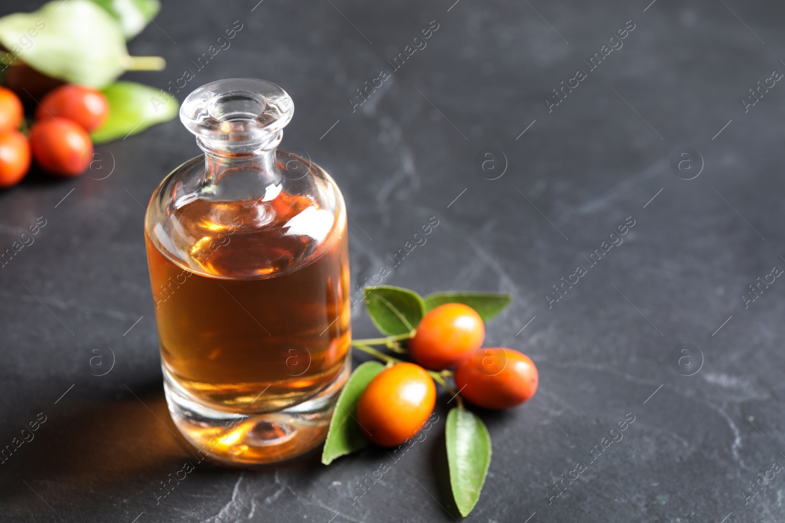 Photo of Glass bottle with jojoba oil and seeds on grey stone table