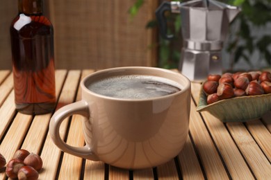 Photo of Mug of aromatic coffee with hazelnut syrup on wooden table, closeup