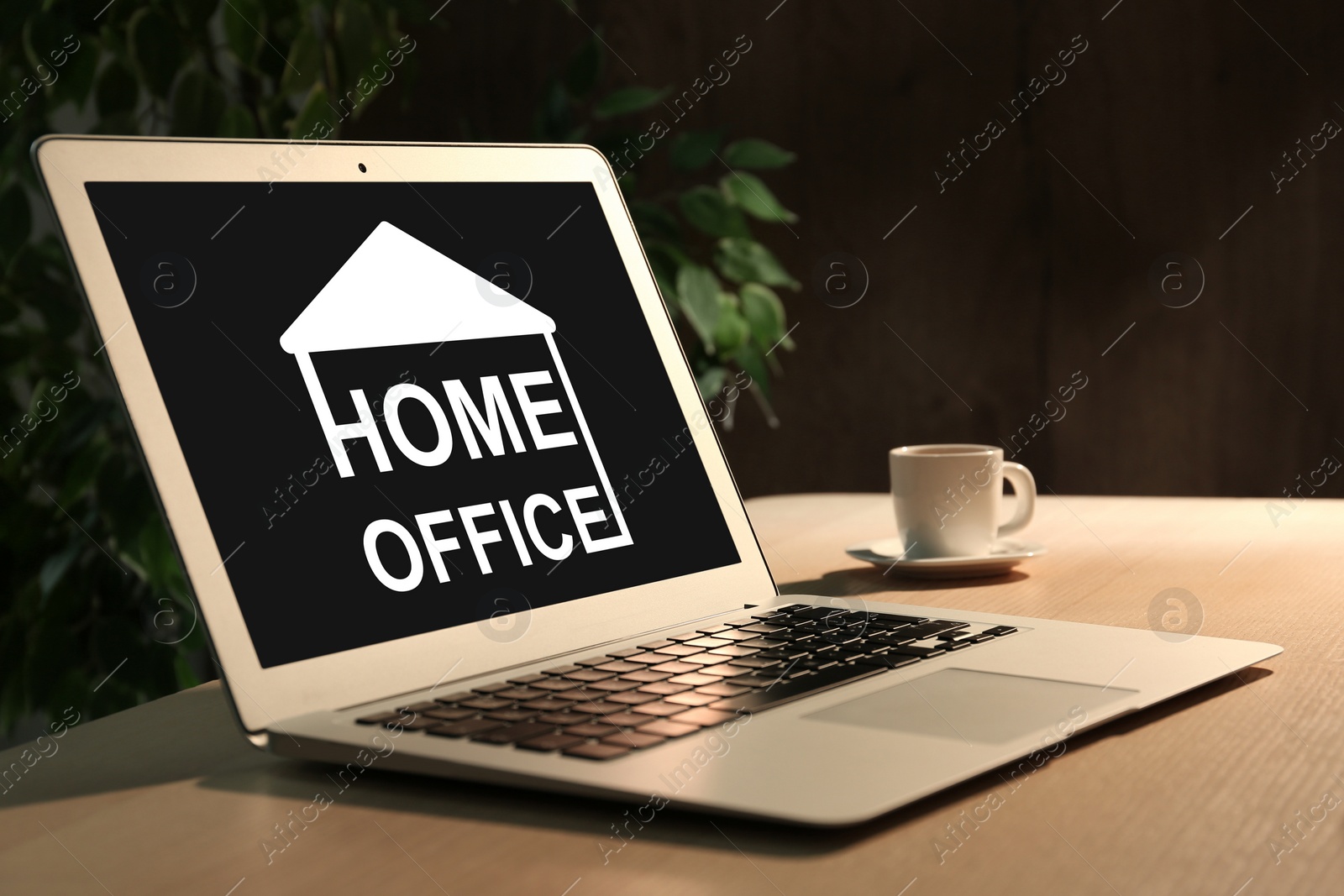 Image of Modern laptop with text HOME OFFICE and cup of coffee on wooden table indoors