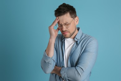 Photo of Man suffering from terrible migraine on light blue background