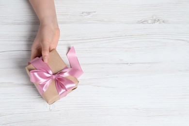 Photo of Woman holding gift box with pink bow at white wooden table, top view. Space for text