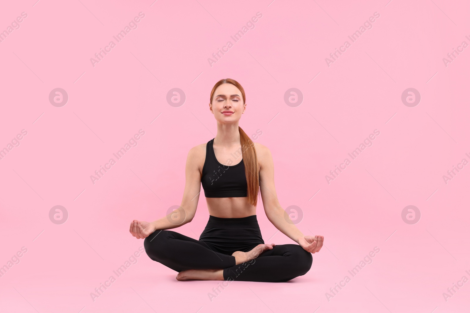 Photo of Beautiful young woman practicing yoga on pink background. Lotus pose