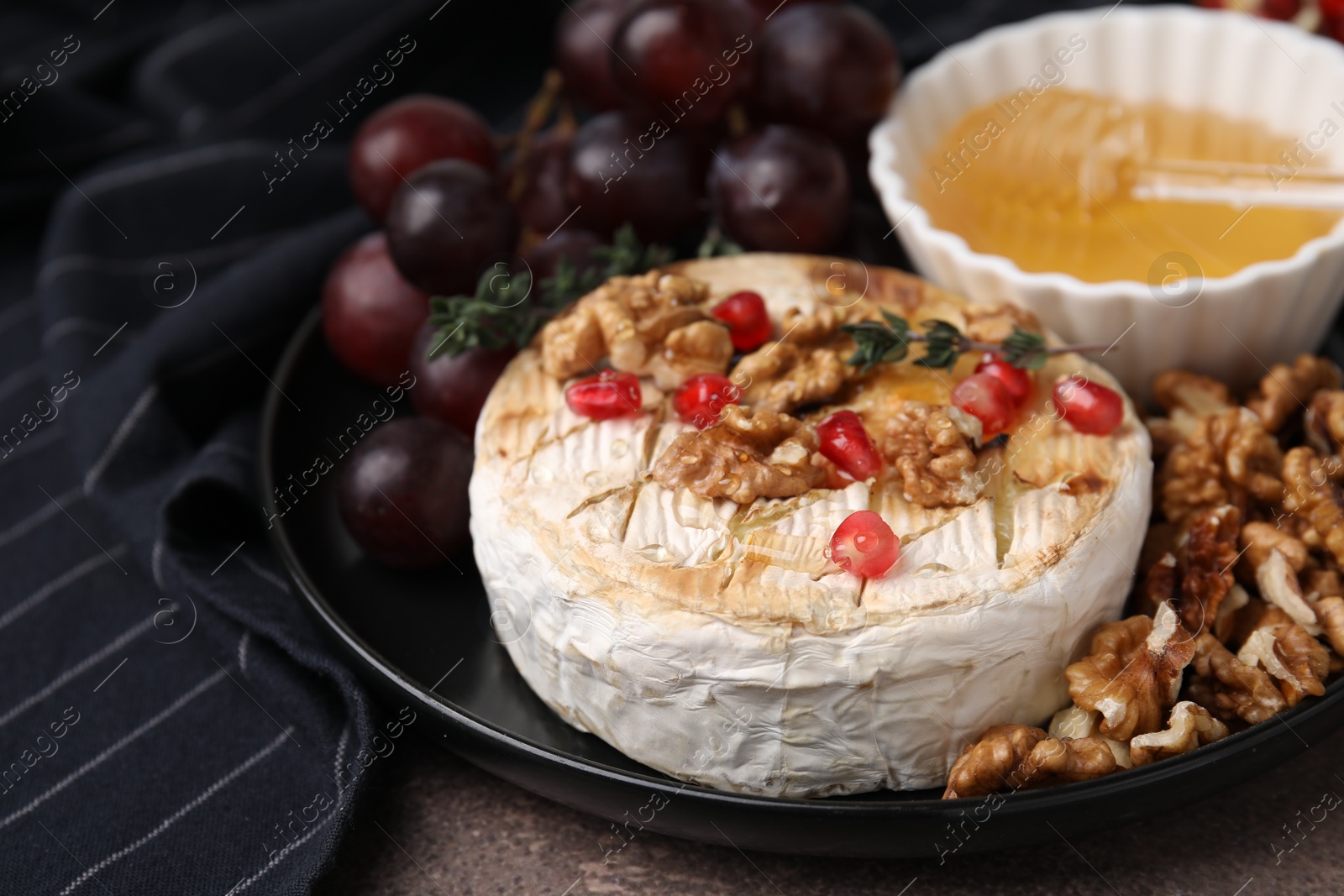 Photo of Plate with tasty baked camembert, honey, grapes, walnuts and pomegranate seeds on table, closeup