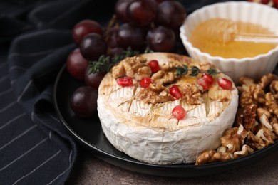 Photo of Plate with tasty baked camembert, honey, grapes, walnuts and pomegranate seeds on table, closeup