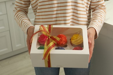 Woman holding box with delicious colorful cupcakes indoors, closeup